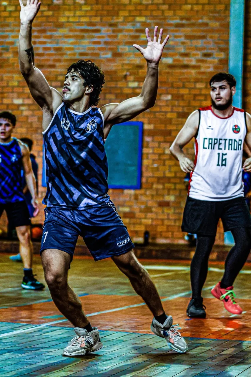 Jogador de basquete da atlética comemorando de braços erguidos durante a partida
