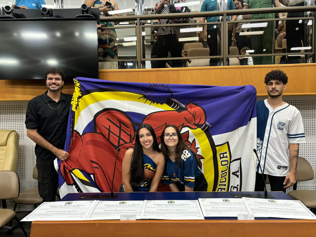 Membros da atlética segurando a bandeira em sessão de homenagem na câmara municipal