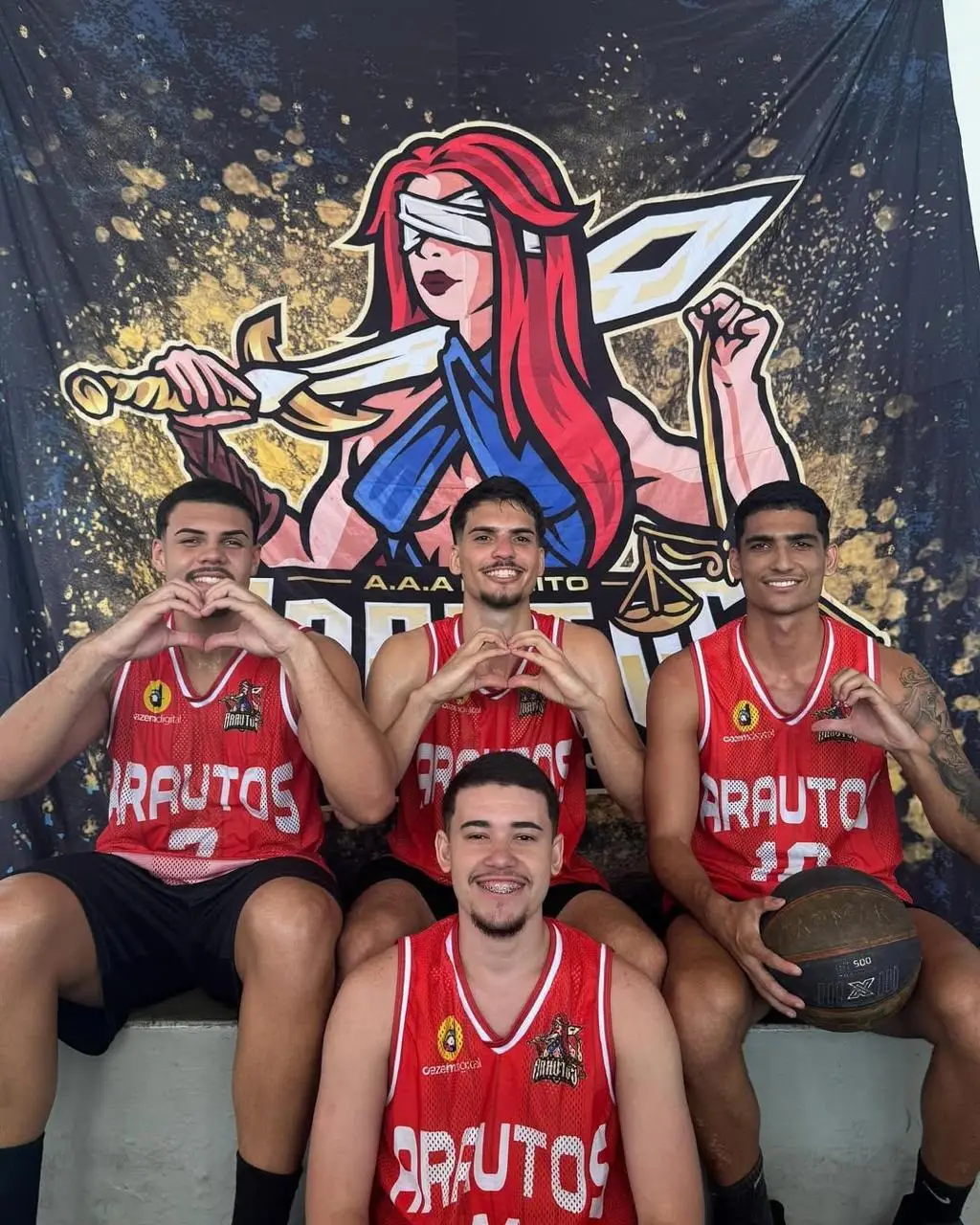 Time de basquete da atlética fazendo coração com as mãos diante do backdrop