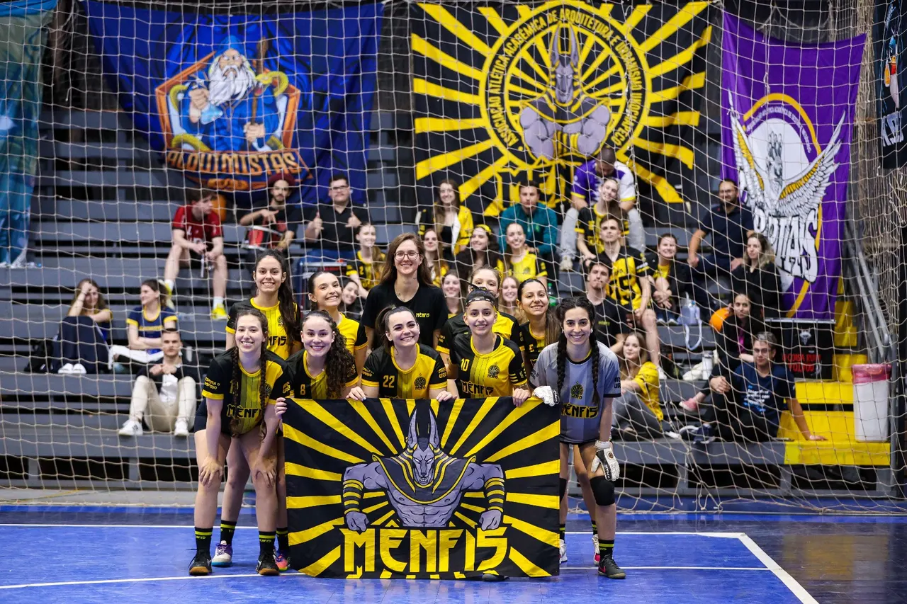 Time feminino de futsal da atlética posando com a bandeira na quadra